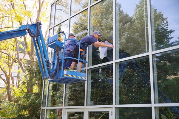 Two people standing in a crane bucket applying bird strike prevention dots to second story windows