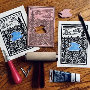 A linoleum cut stamp of a lake vista with two prints and block printing supplies